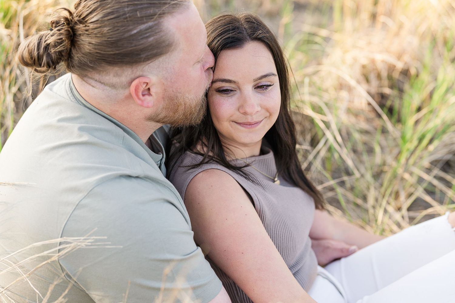 Man tenderly kissing woman's cheek as she smiles softly in a golden field.