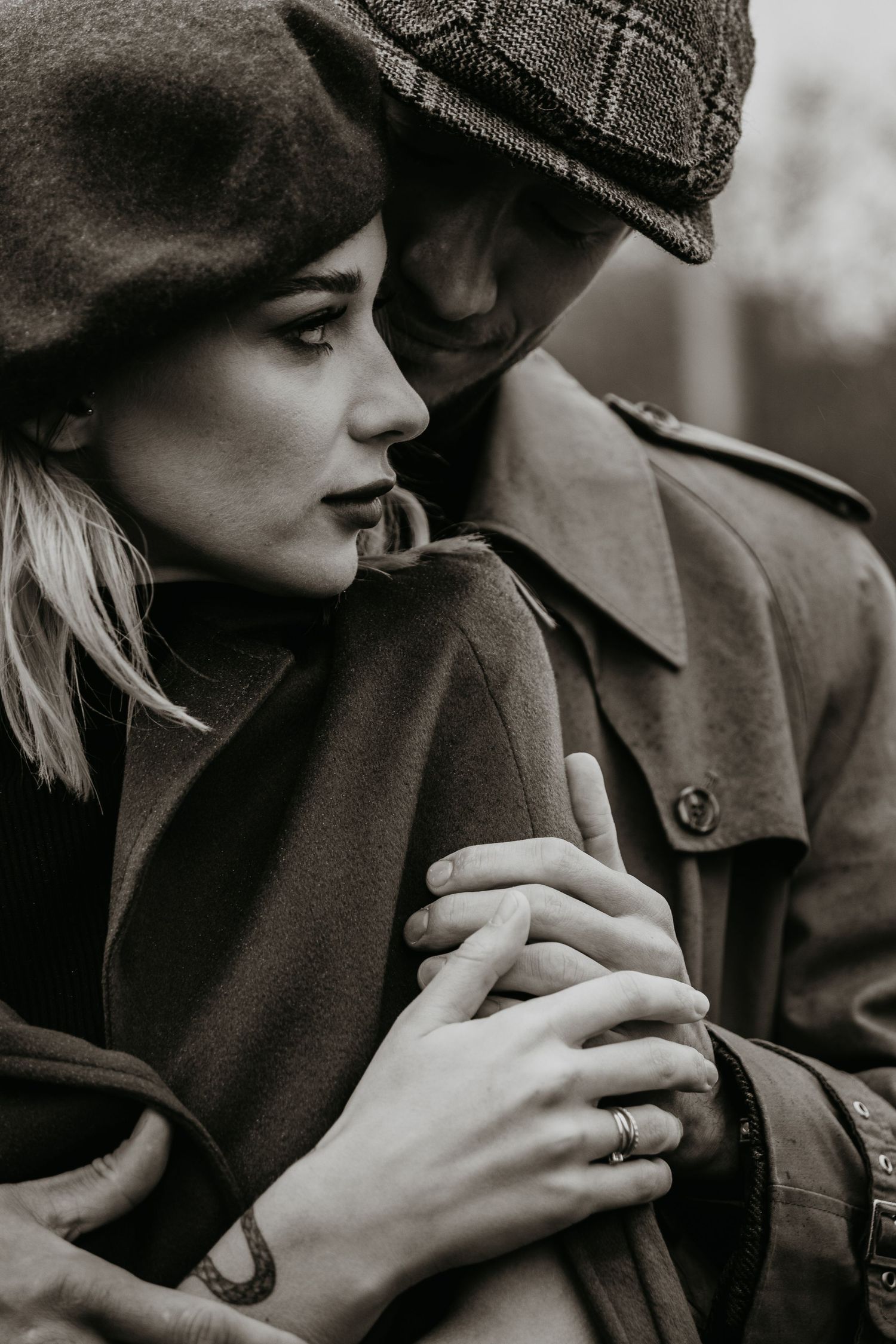 A couple in winter coats and hats share an intimate moment in black and white sepia tones.