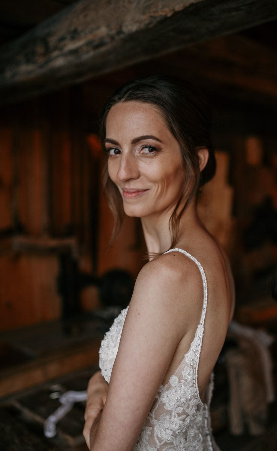 A smiling bride in a lace wedding dress poses in a rustic barn setting.