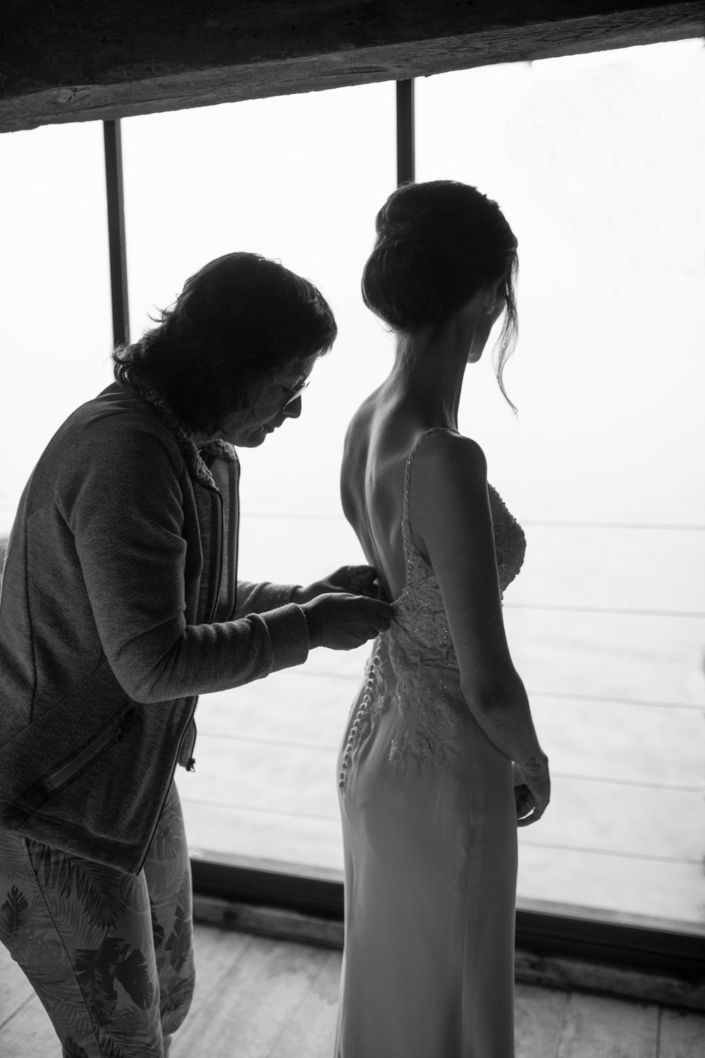 Black and white silhouette of a person fastening the back of a bride's elegant wedding gown.