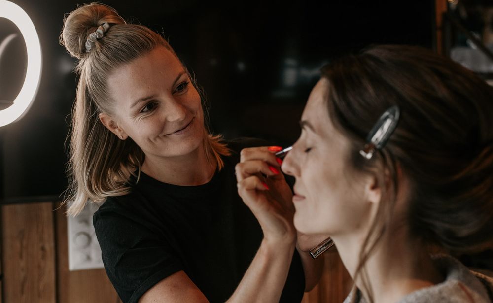Professional makeup artist applying eye makeup to bride under ring light before wedding ceremony.