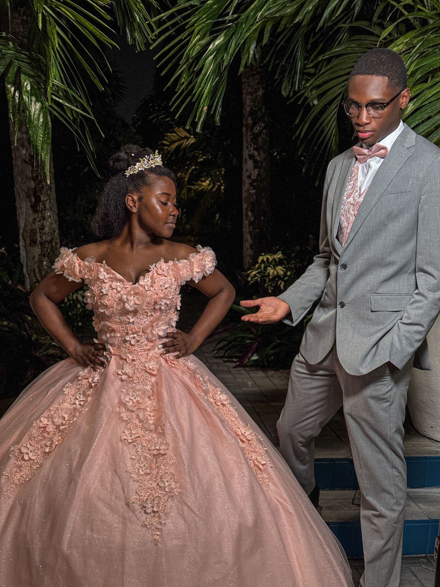 An elegant scene with a peach ballgown and grey suit against a tropical palm backdrop.