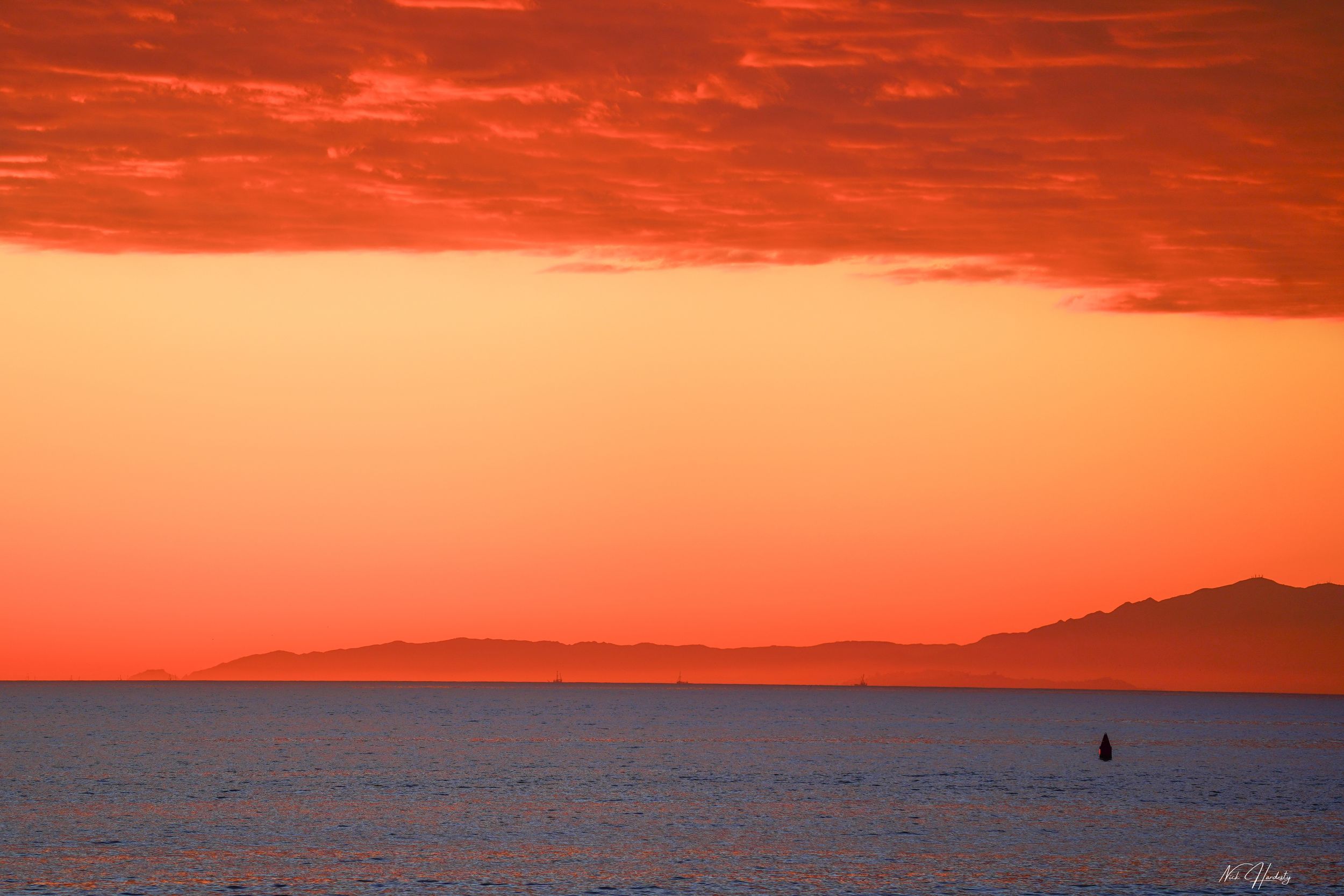 Bold orange sunset over the Ventura coast, with the sun dipping low near the horizon and the sky lit in warm, glowing tones. Ocean reflects