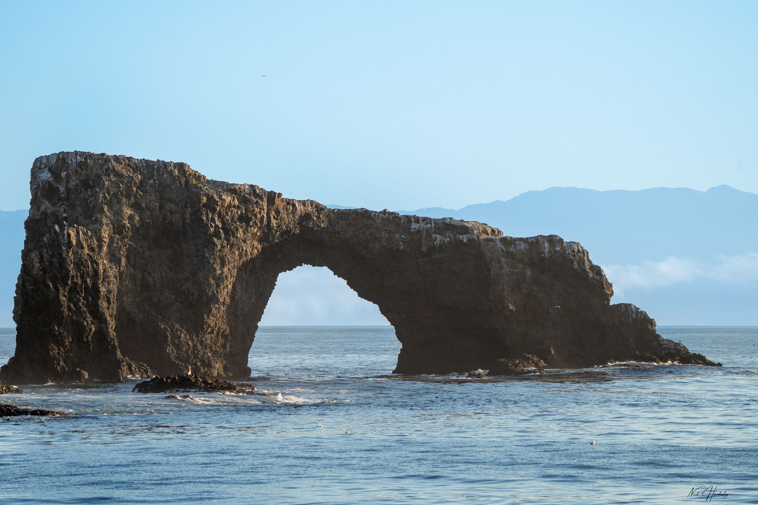 Waves crashing through Anacapa Arch with mist and low clouds in the distance.