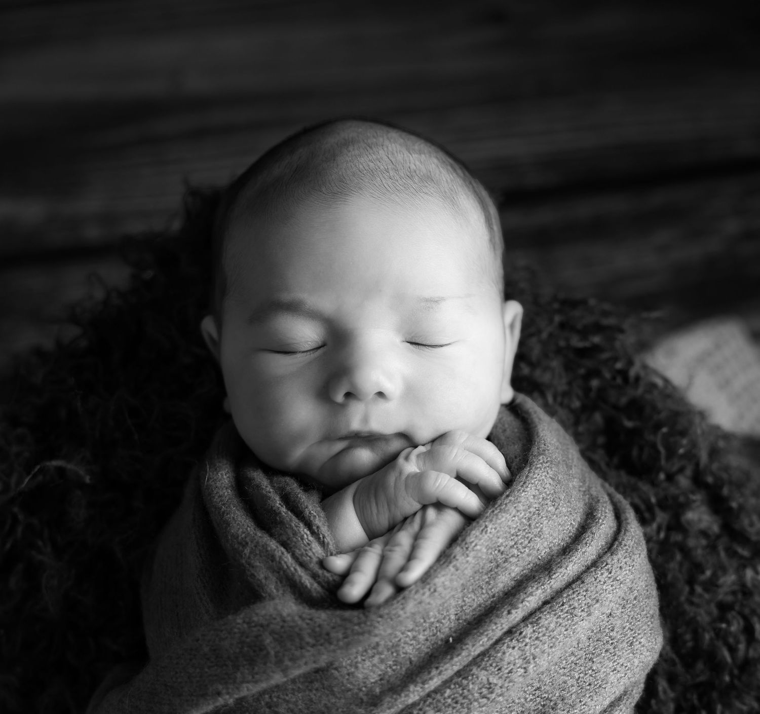 Peaceful sleeping newborn swaddled in soft blanket against dark background.