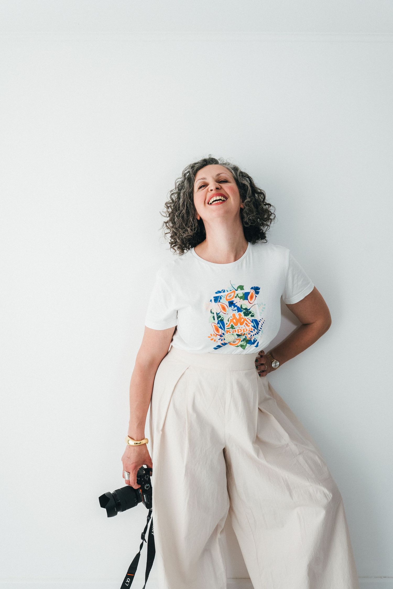 Carmen Palermo, photographe à Metz,Thionville,Luxembourg, debout en studio, souriante, appareil photo à la main, style naturel et lumineux.