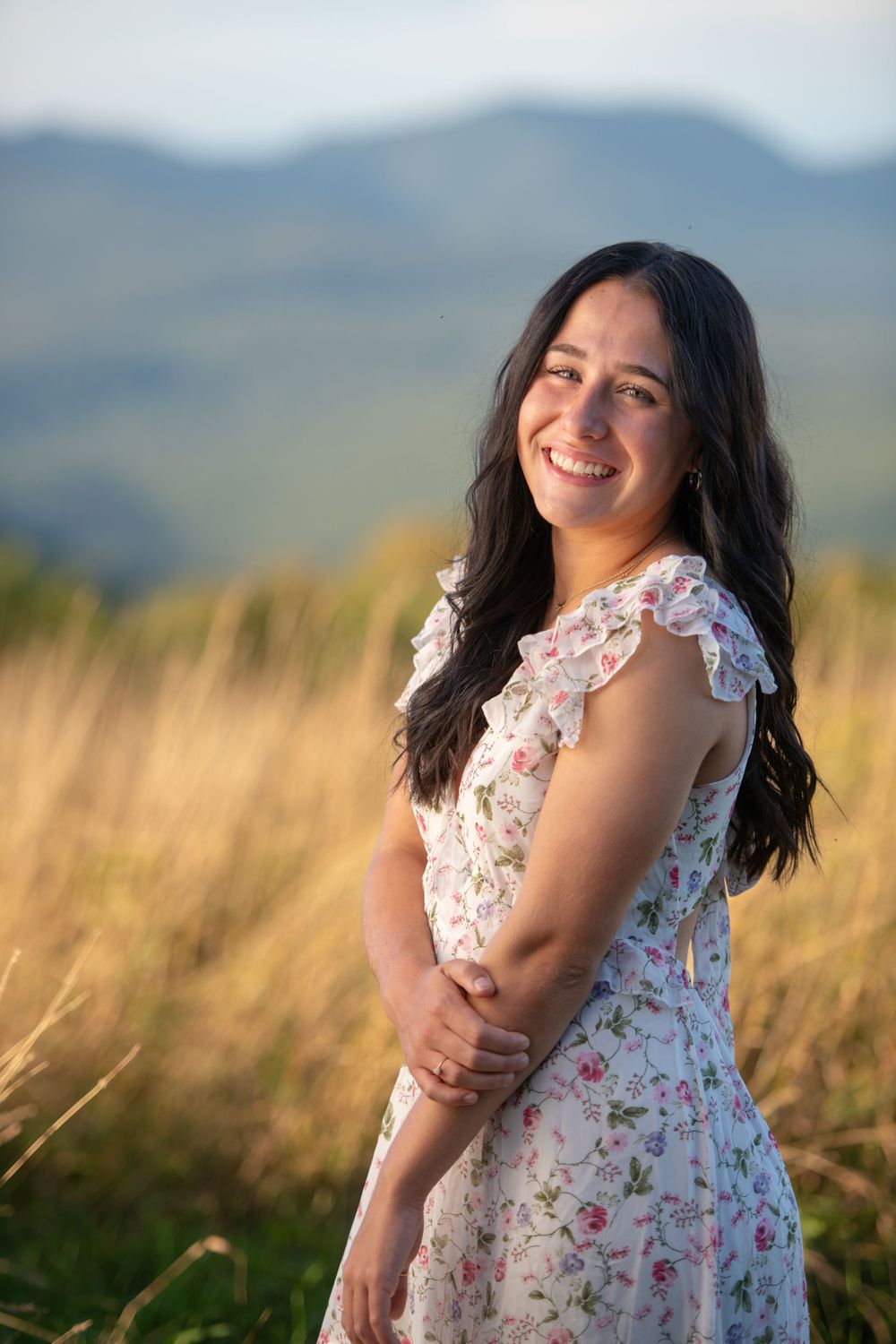 A floral dress is worn outdoors against a mountain backdrop during golden hour.
