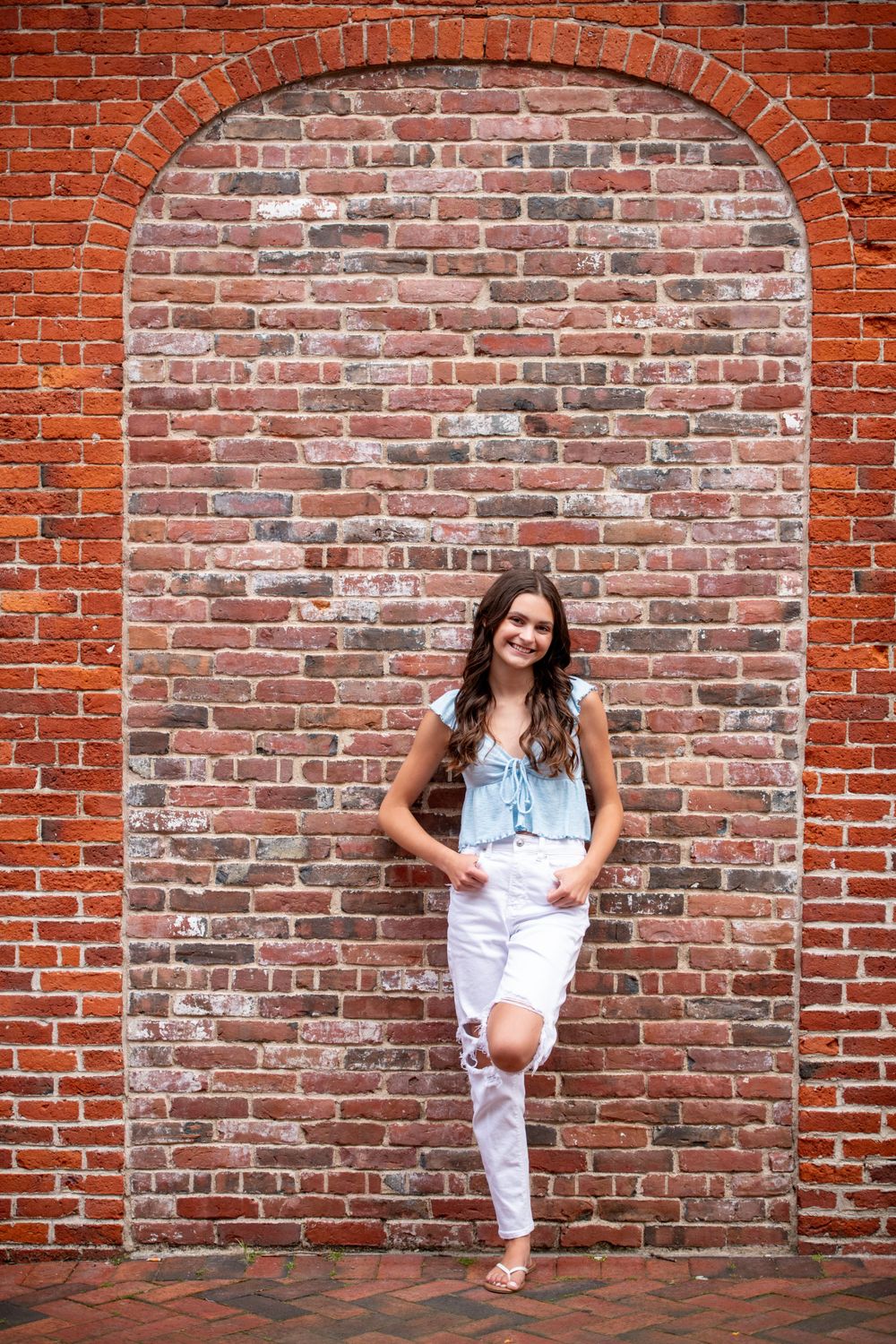 A casual denim outfit frames perfectly within a red brick archway.
