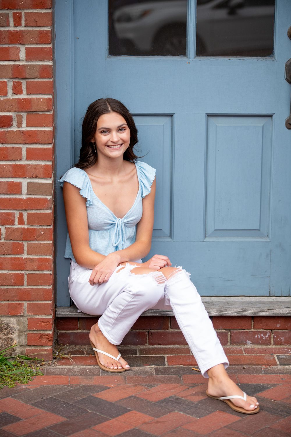 Young person in a white dress sitting on brick steps with a light blue door in the background.