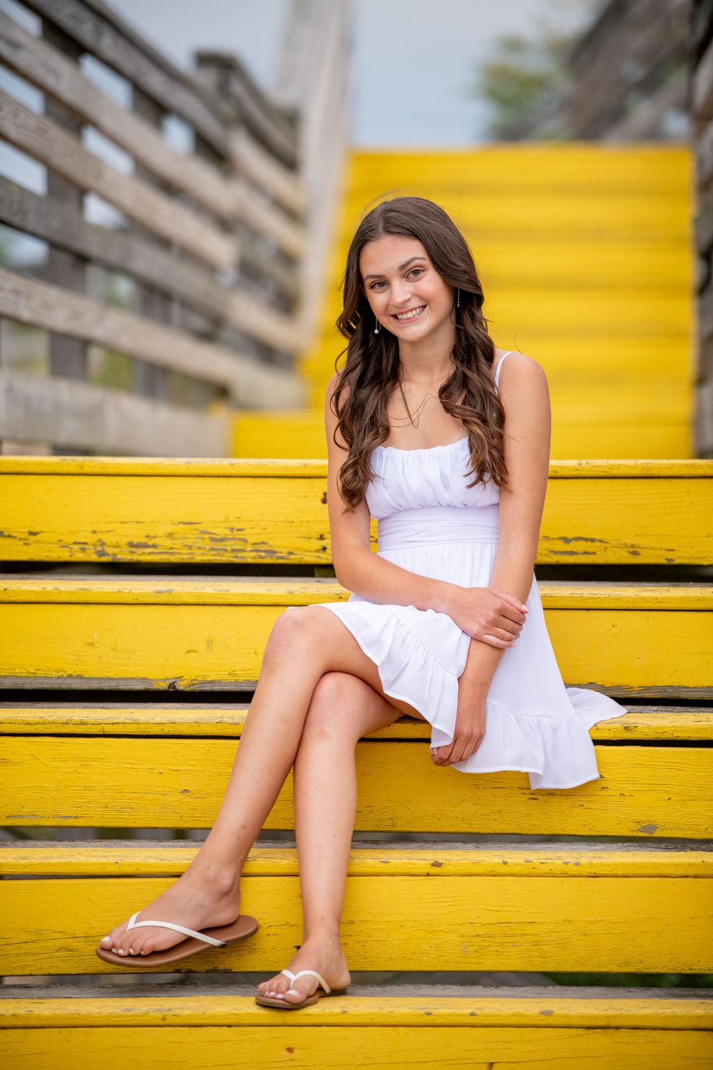 Series of relaxed poses on bright yellow bleachers in a white summer dress.