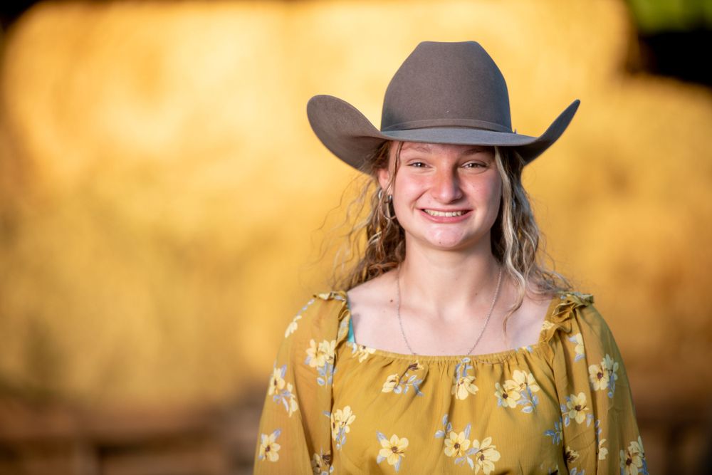 Portrait series in yellow dress and cowboy hat against warm sunset lighting.