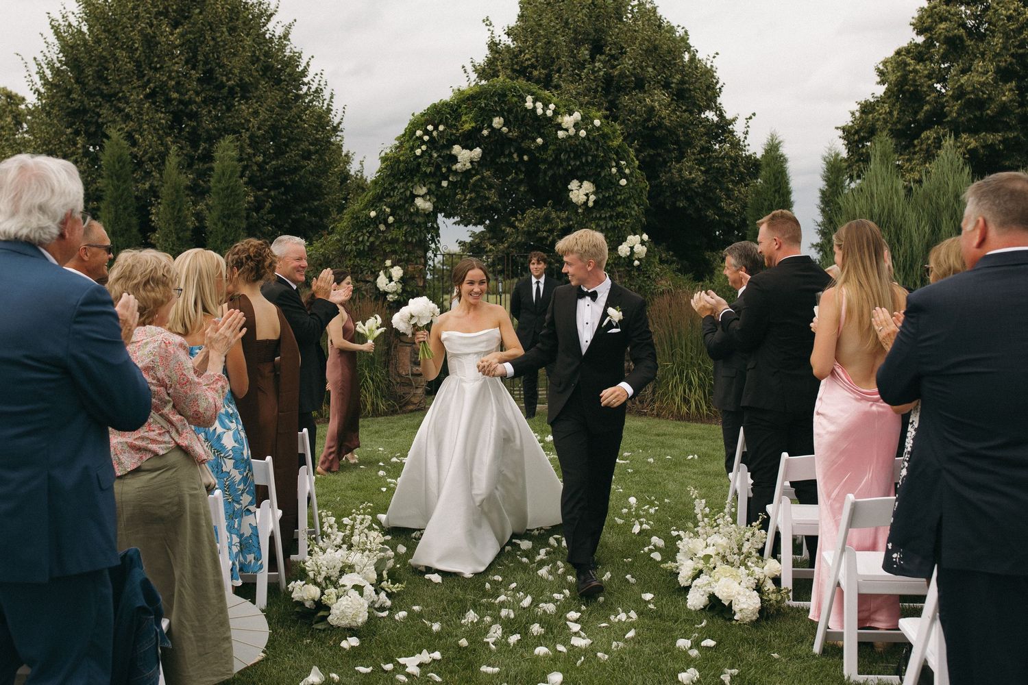 An outdoor wedding ceremony with white flower petals scattered along the aisle.