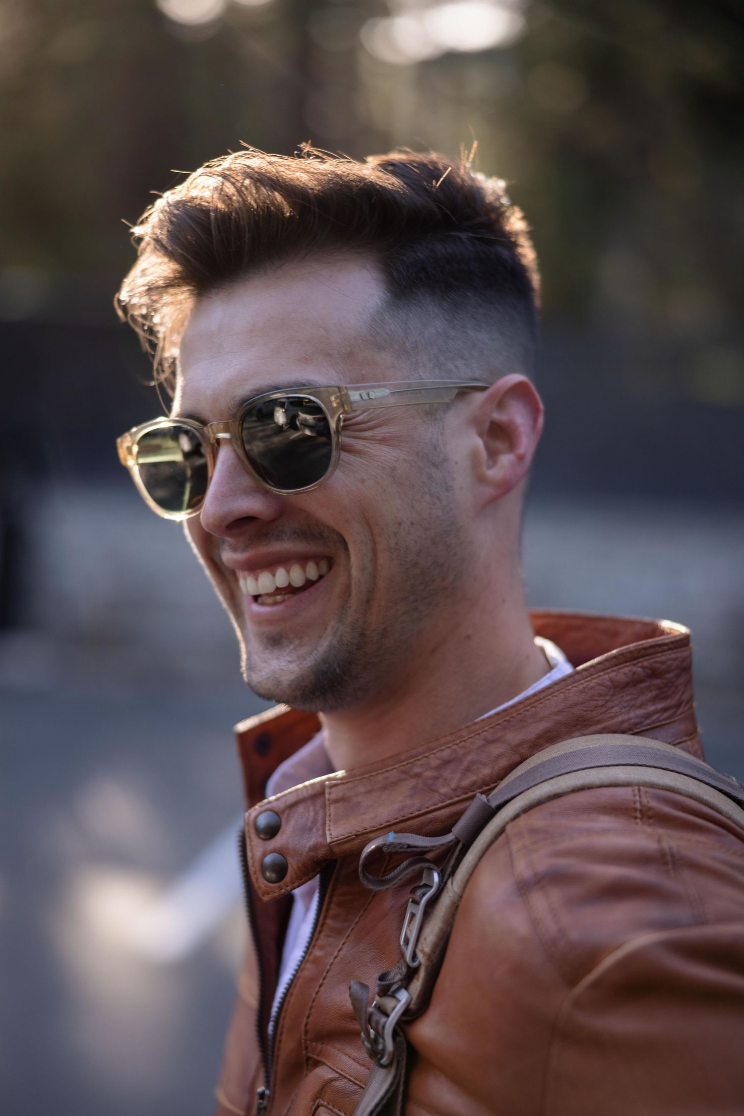 Portrait of person in brown leather jacket and sunglasses with natural lighting.