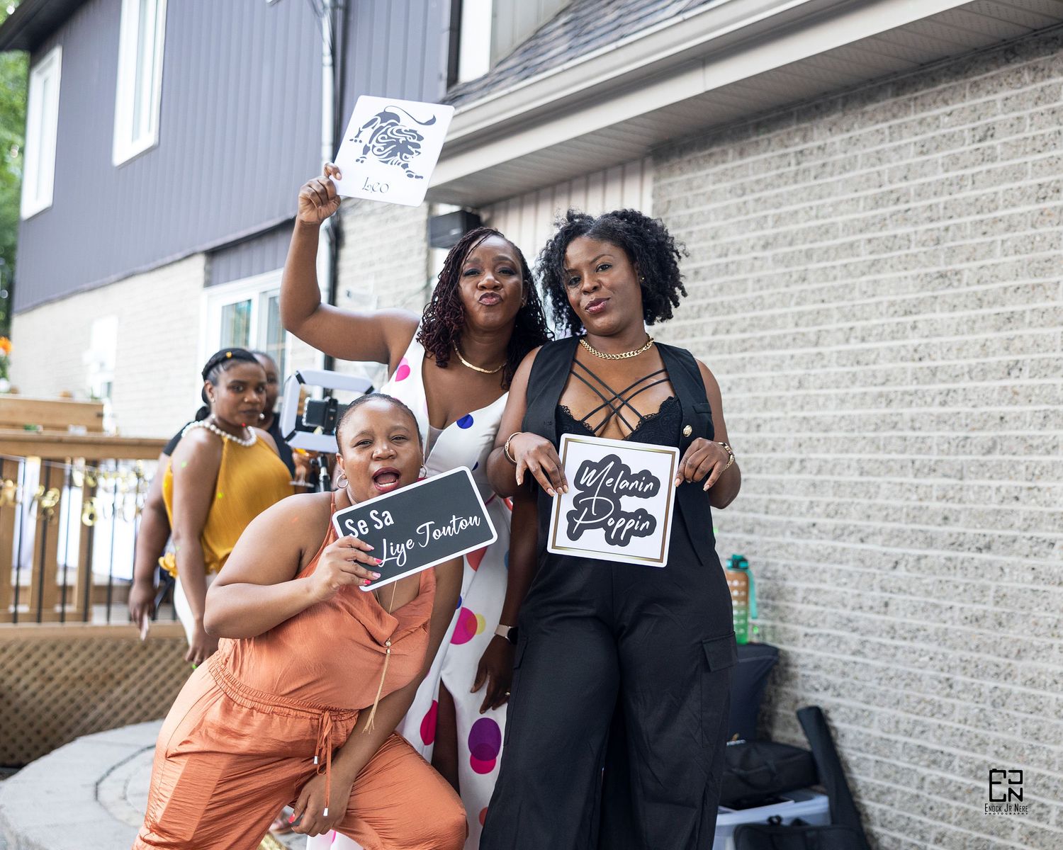 Group celebrating together outdoors while holding up signs and artwork near white brick wall.