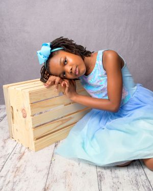 Professional photo series showing a flowing light blue gown against wooden crates with a gentle pose.