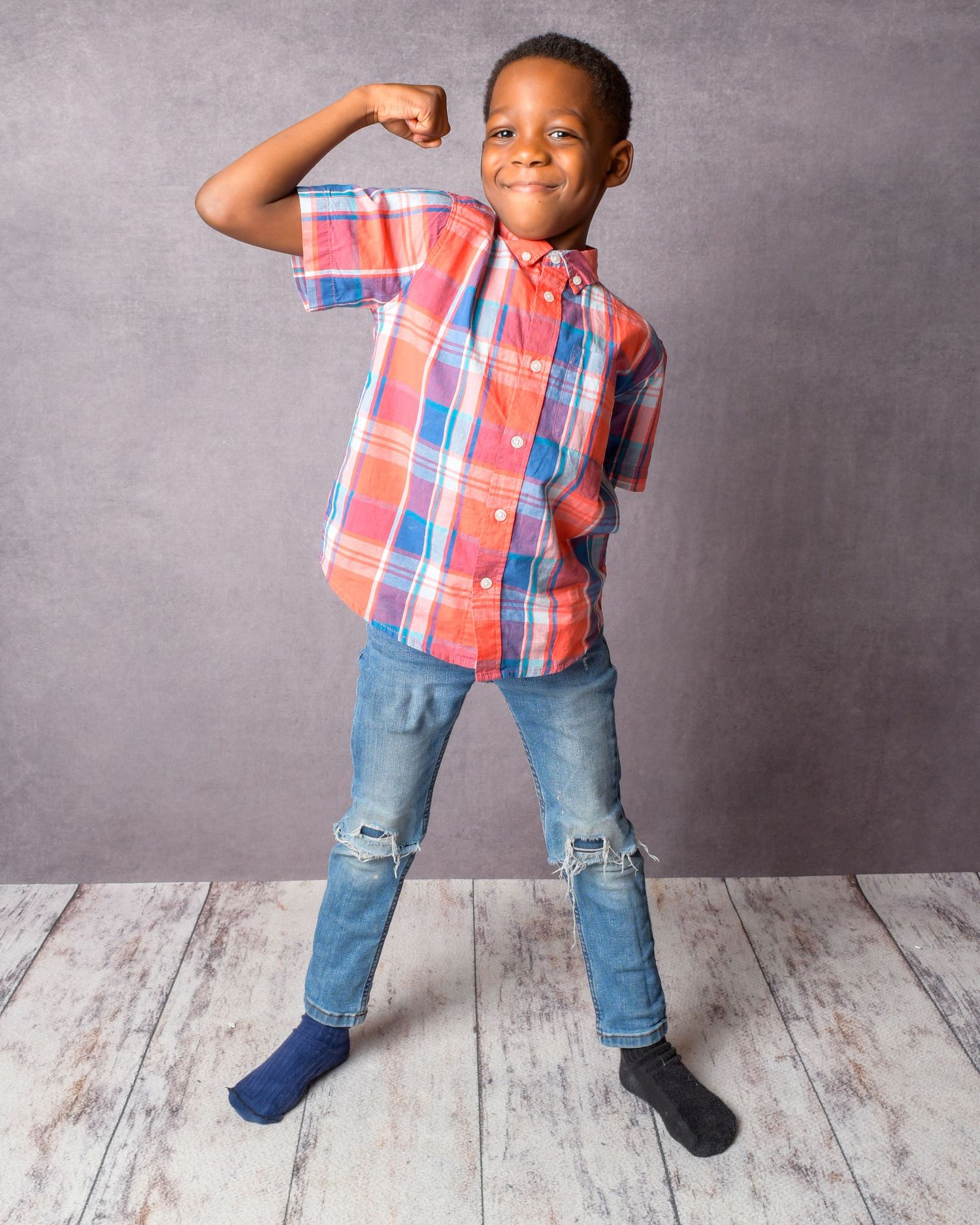 Young person in plaid shirt and jeans strikes fun poses against grey studio background.
