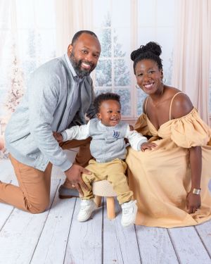 Family sharing playful moments together during indoor photo session on white wooden floor.