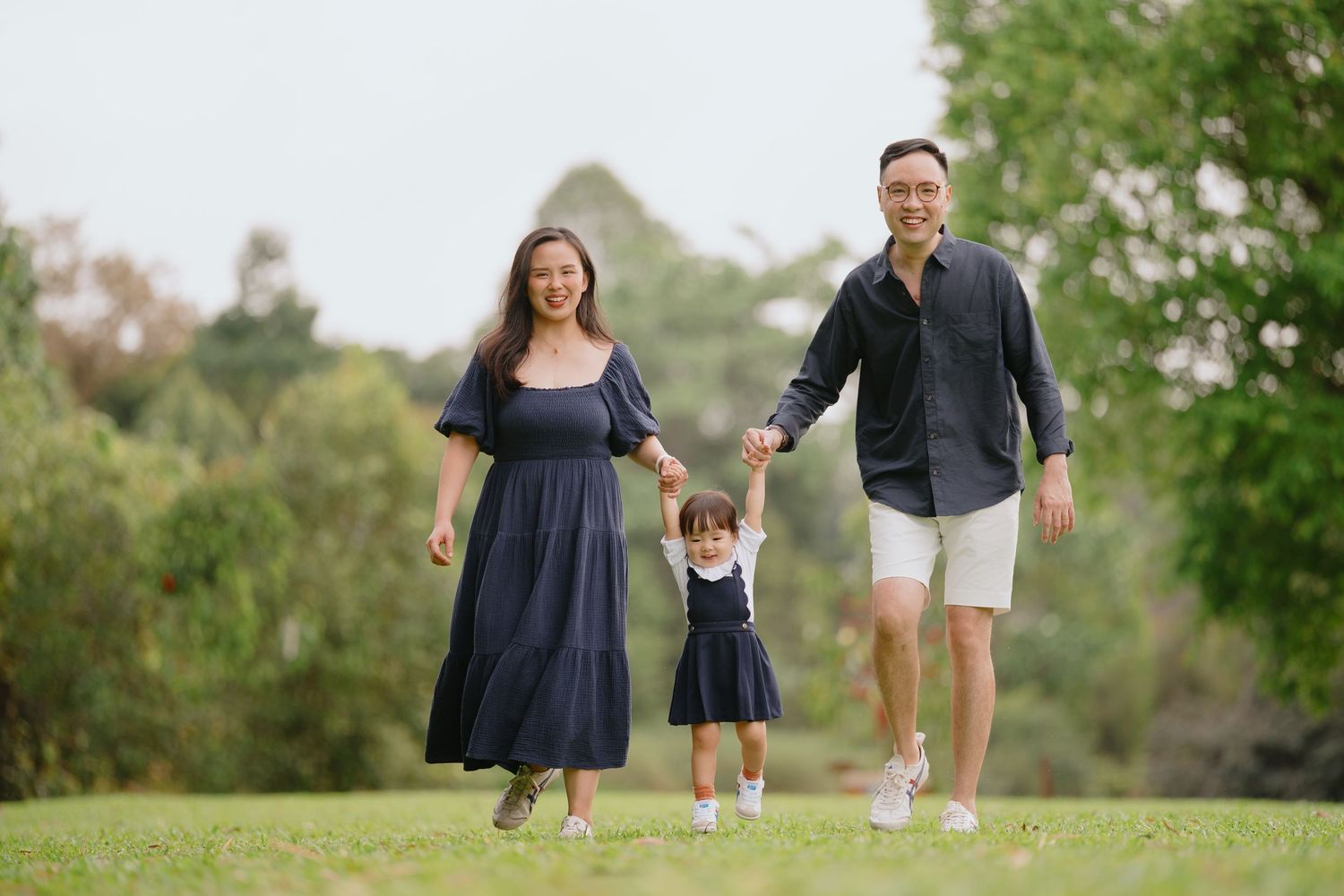 A happy family of three plays and runs together in a lush green park during a sunny afternoon.