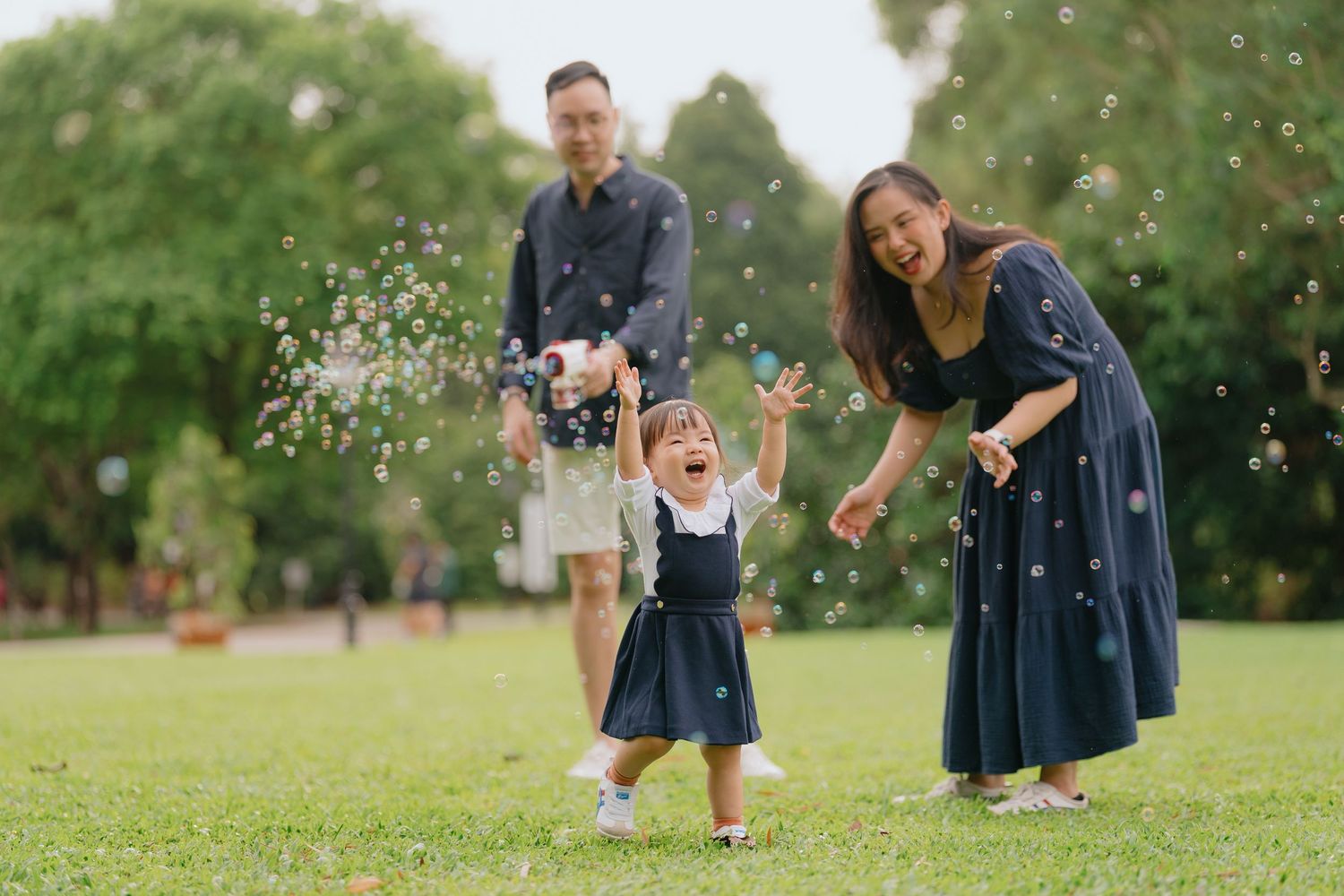 Children in matching navy blue dresses play together on green grass in a park setting.