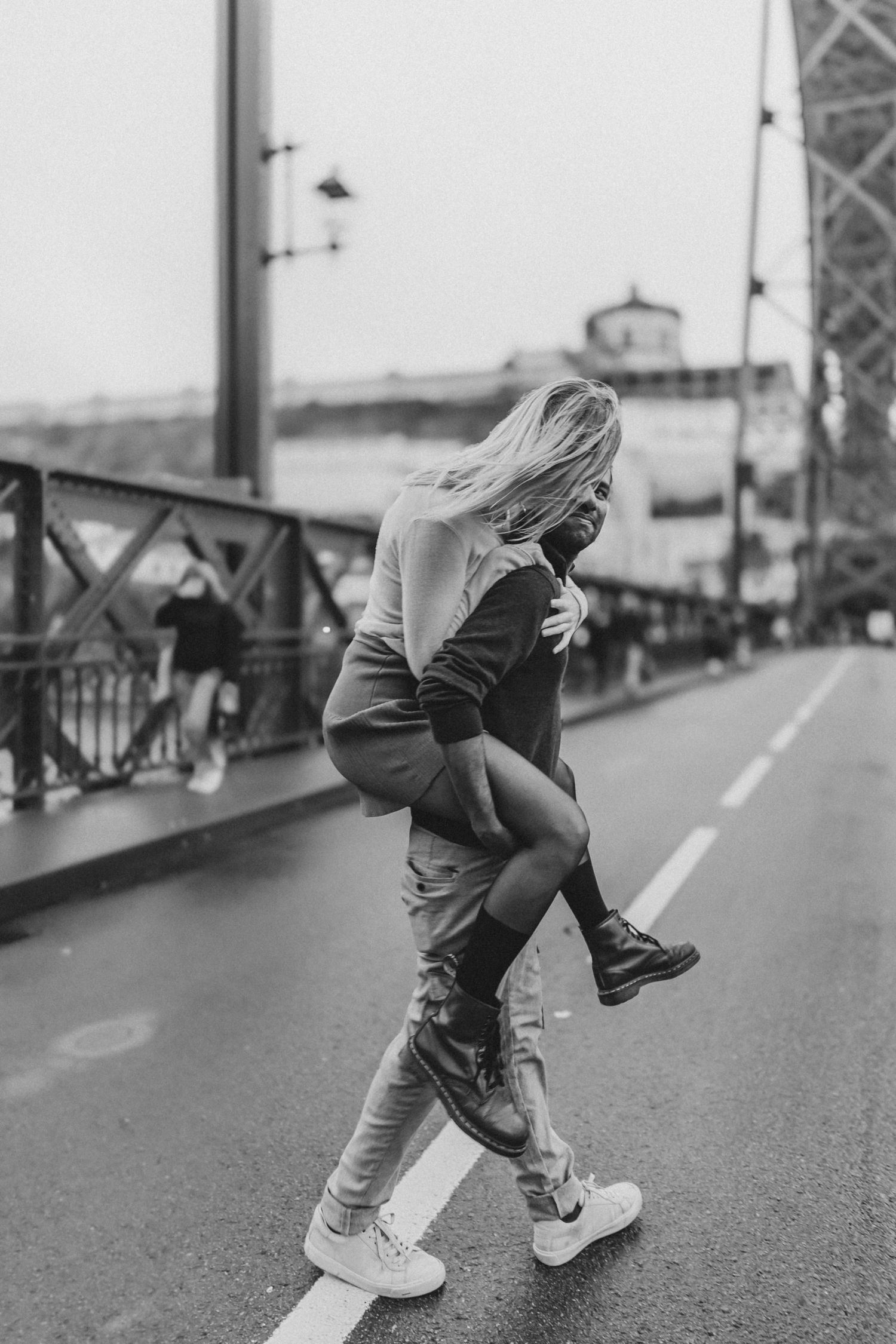 Black and white photo of playful couple embracing on urban bridge in Porto