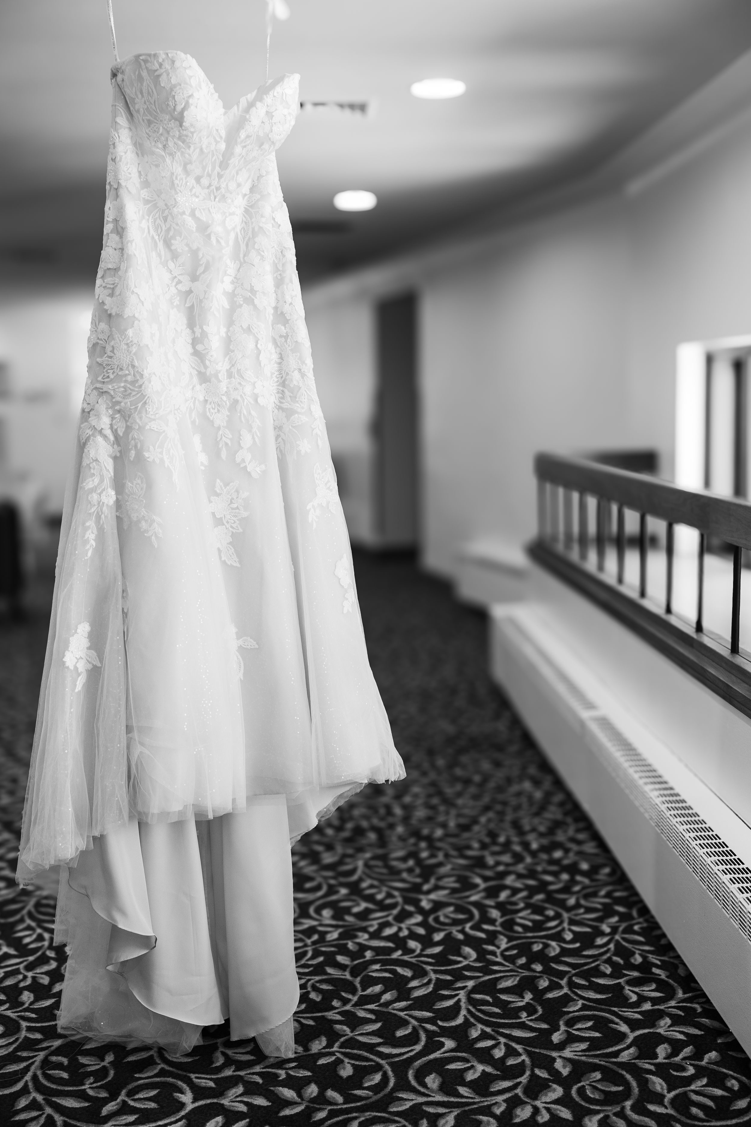 Wedding dress hanging to the side of a small window in black and white.