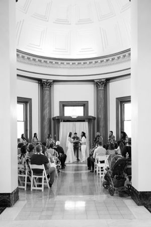 Wide angle of the inside of the ceremony space with the bride and groom standing at the alter in black and white.