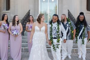 Bride and groom walking and laughing with their bridal party in an outdoor urban setting.