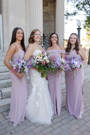 Bride with her bridesmaids smiling softly outside an urban city building.