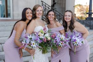 Bride and her bridesmaids sharing a group hug with a big smile standing outside an urban city building.