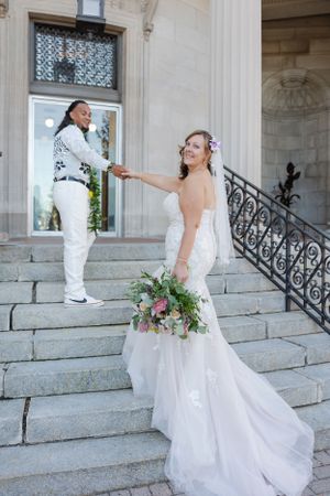 Bride and groom on a set of stairs outside an urban city building holding hands walking up towards the door.