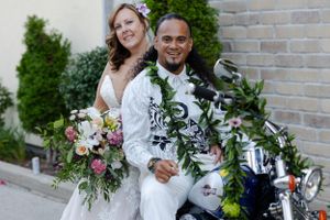 Groom sitting and bride leaning again a motorcycle smiling comfortably.