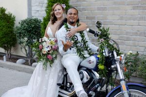 Groom sitting and bride leaning again a motorcycle smiling comfortably.