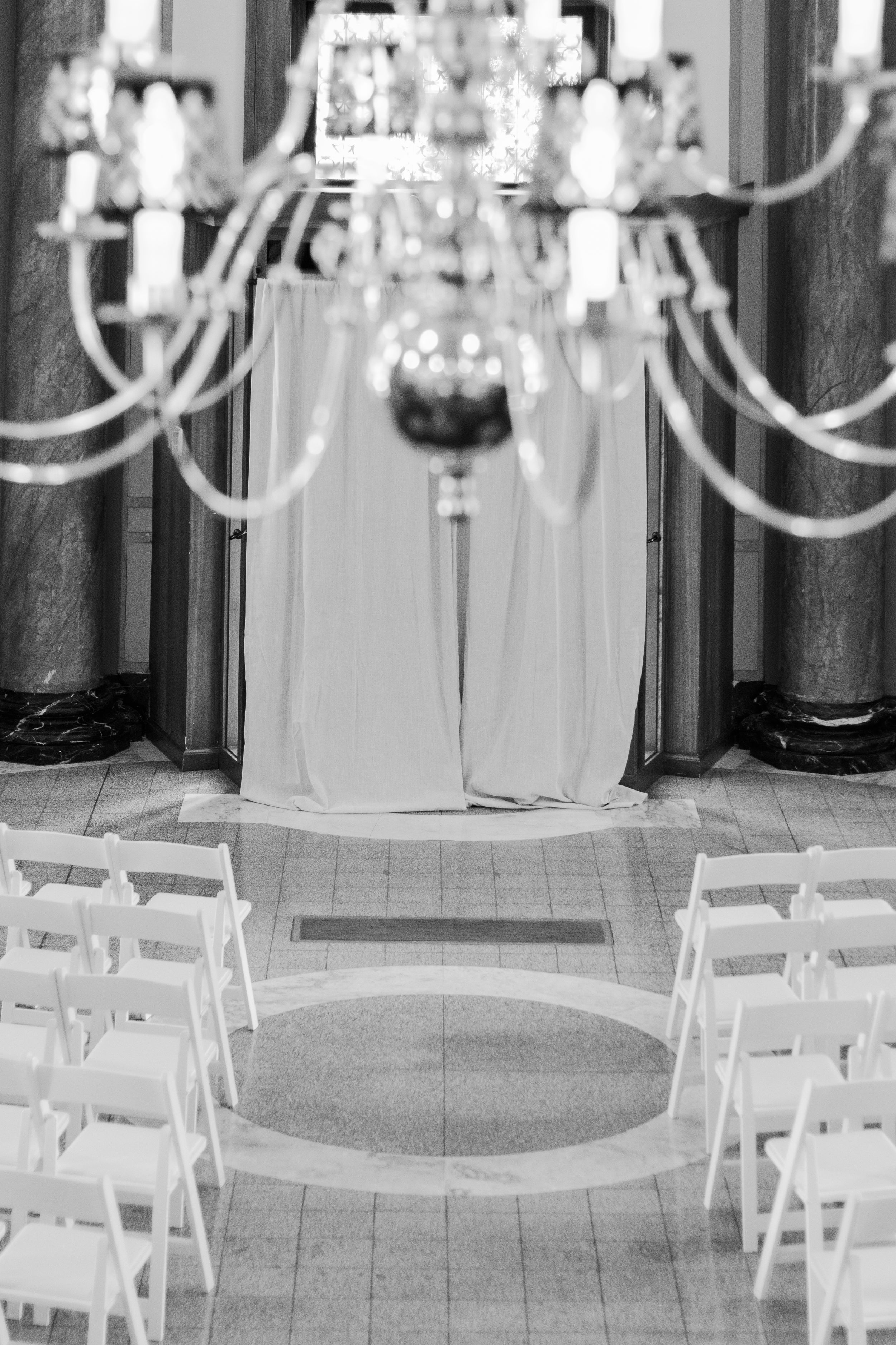 Black and white empty ceremony space with a chandelier hanging high above the space.