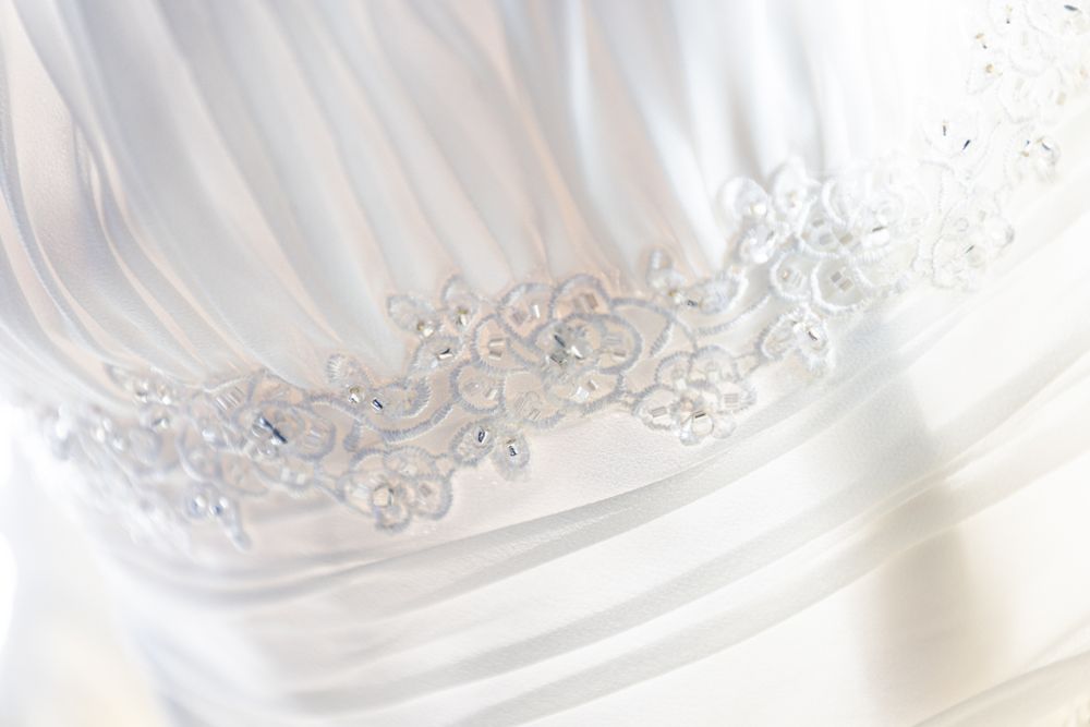 Delicate beaded embroidery detail on white wedding dress fabric.