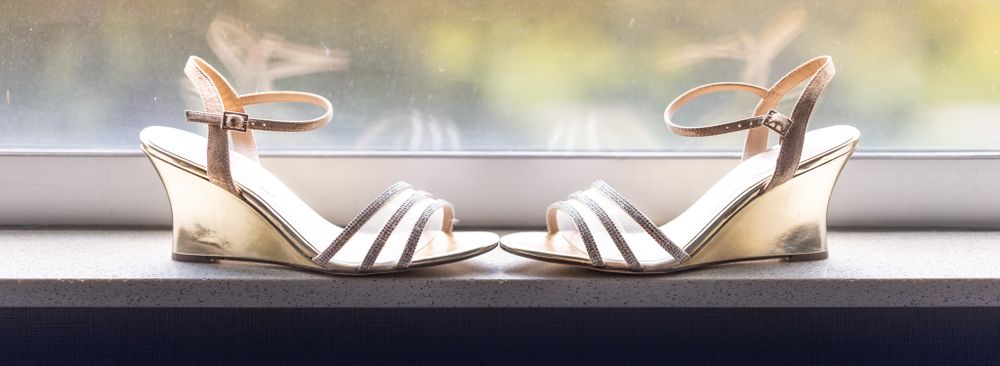 Elegant white wedding sandals with ankle straps displayed on windowsill.