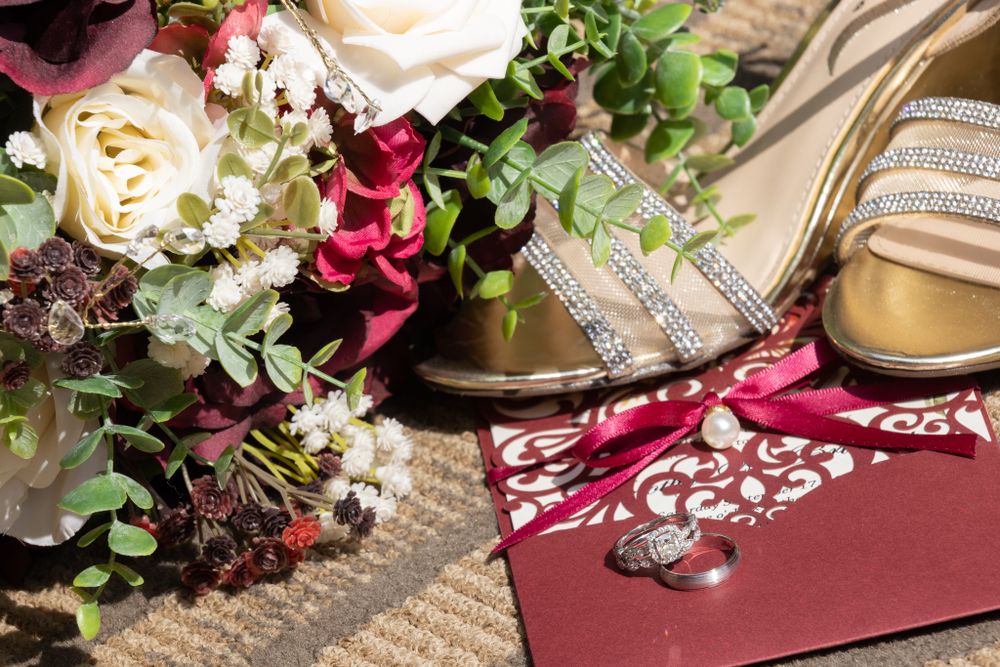 Wedding accessories arranged with burgundy roses and floral invitation on textured surface.