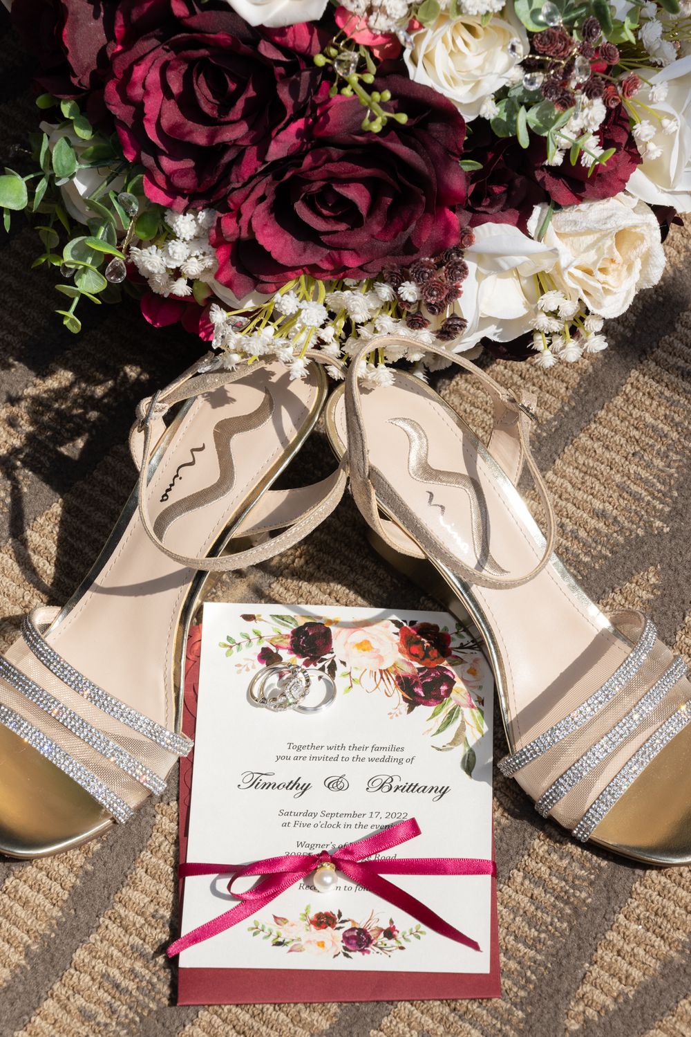 Wedding invitation with burgundy roses and beige sandals in flatlay composition.