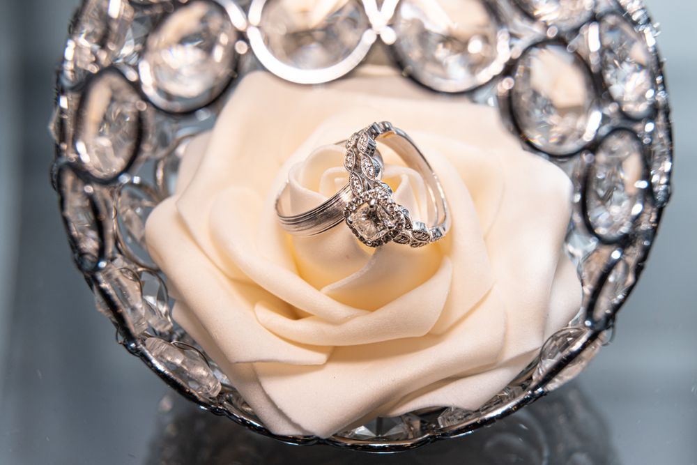 Diamond engagement ring displayed on a pale rose surrounded by crystal decorations.