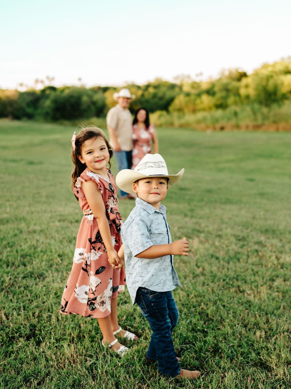 Two young children play and chase each other in a grassy field on a sunny afternoon.