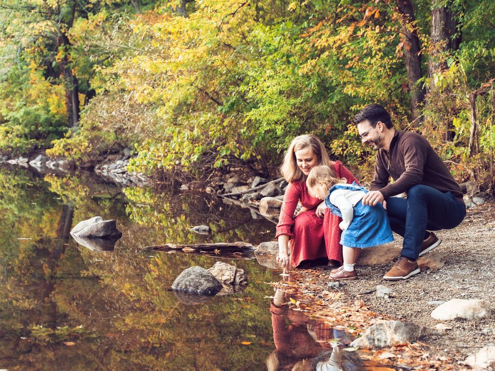 People sitting by a peaceful stream in autumn woods while enjoying outdoor activities together at Menotomy Rocks Park in Arlington, MA.