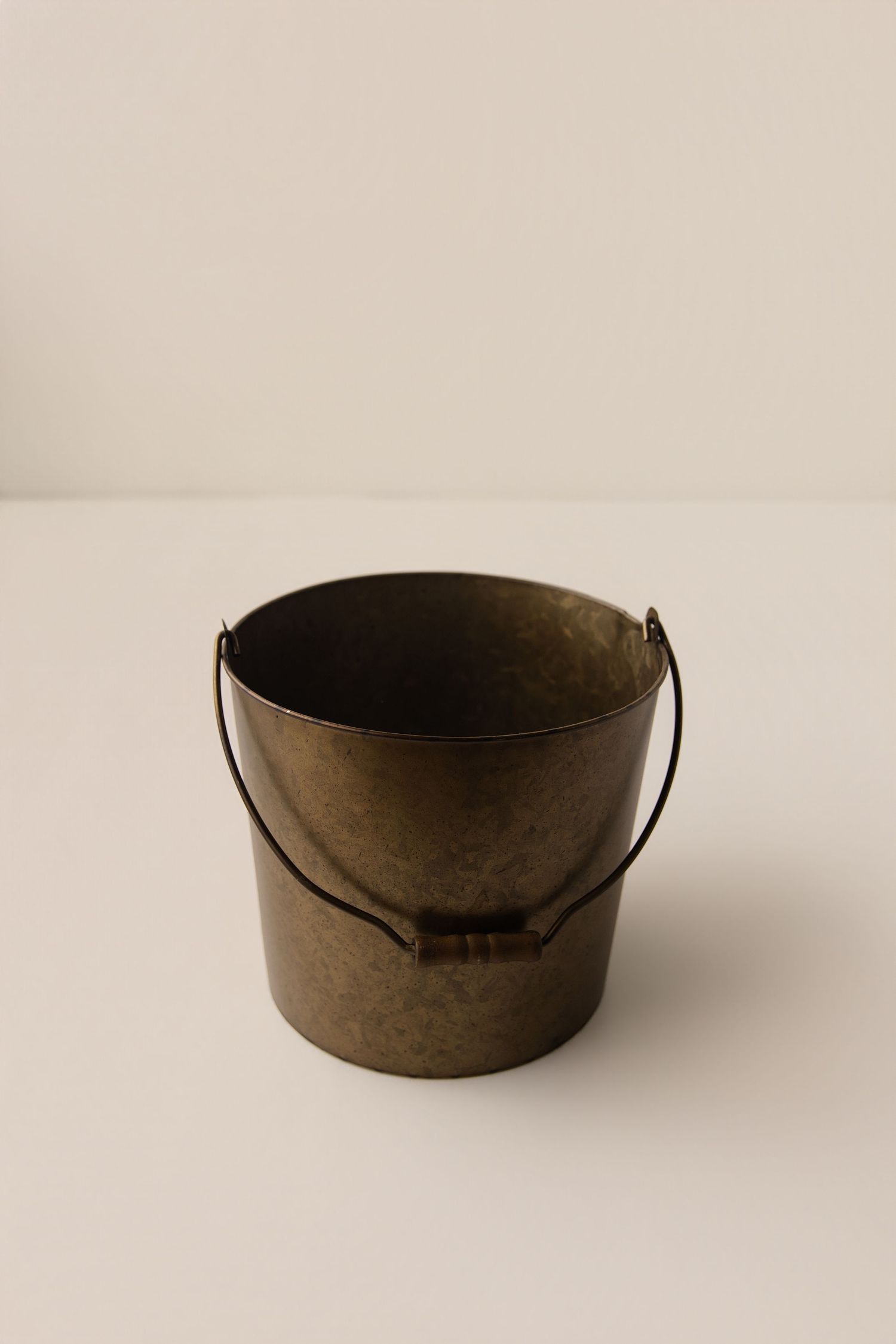 Antique brass metal bucket with wire handle on white surface.