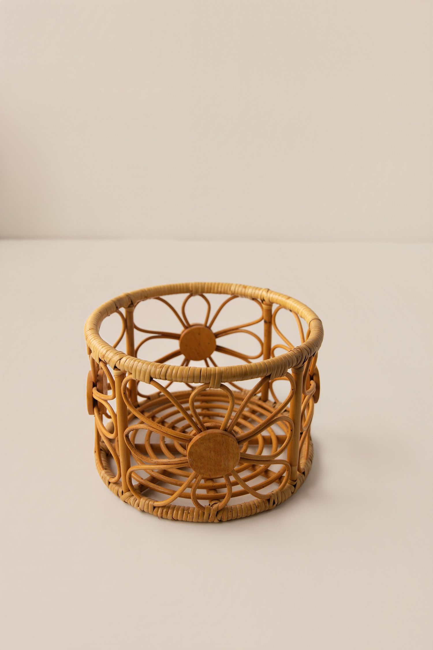 Handwoven rattan basket with intricate floral cutout design, natural tan color, cylindrical shape on white surface.