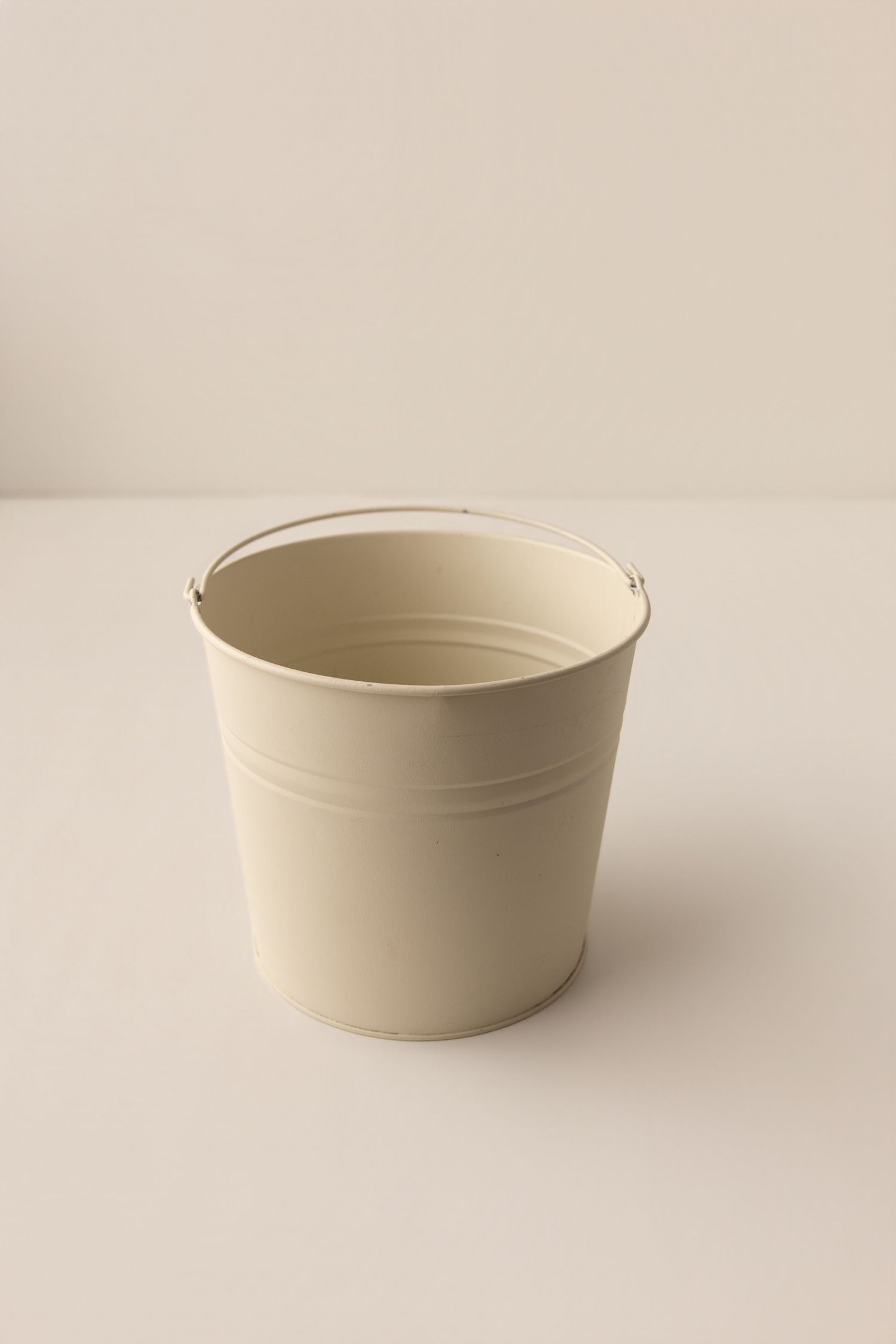 Cream-colored metal bucket with handle on a neutral background, perfect for storage or planting.