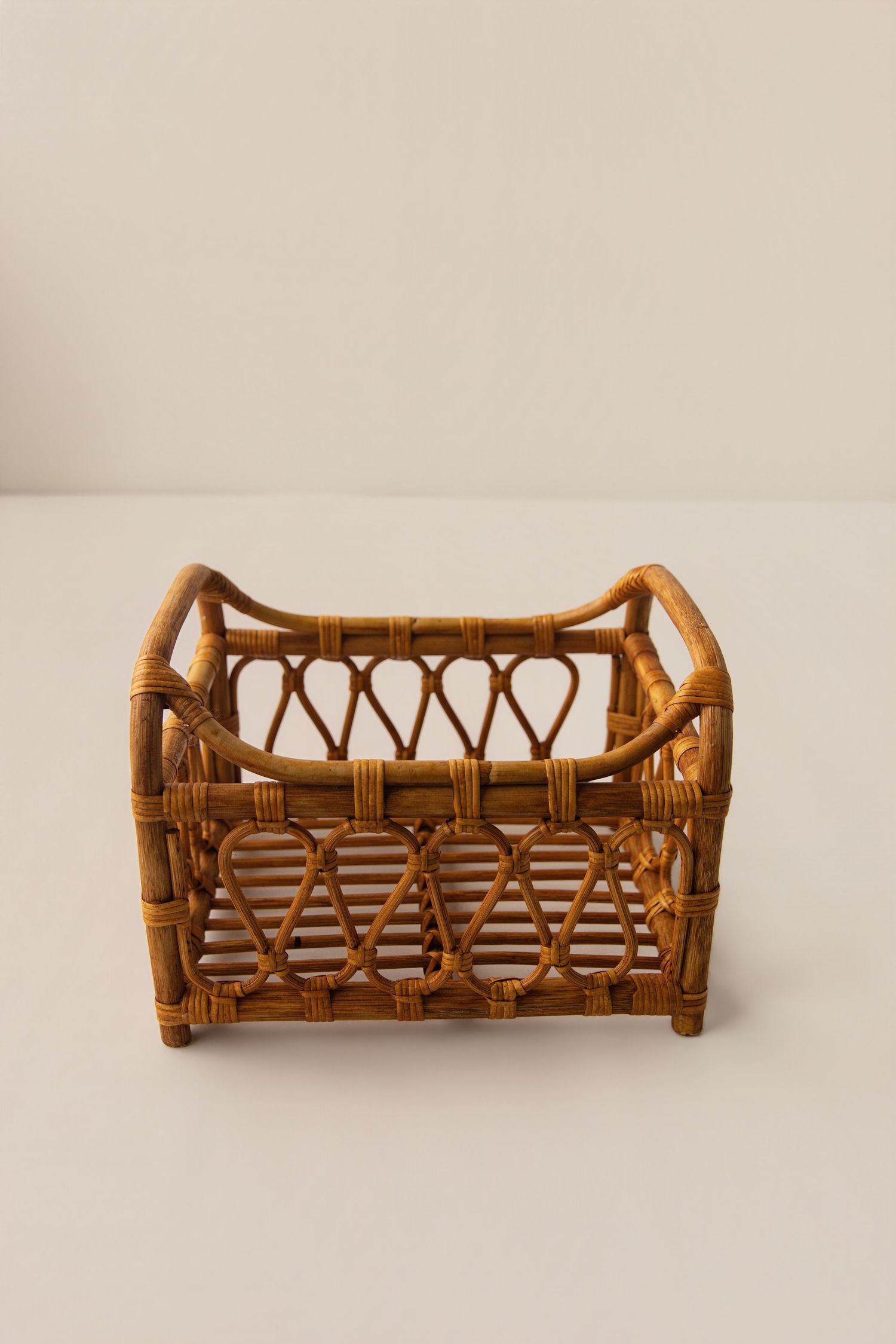 Handwoven rattan storage basket with decorative lattice pattern and curved handles on a neutral background.