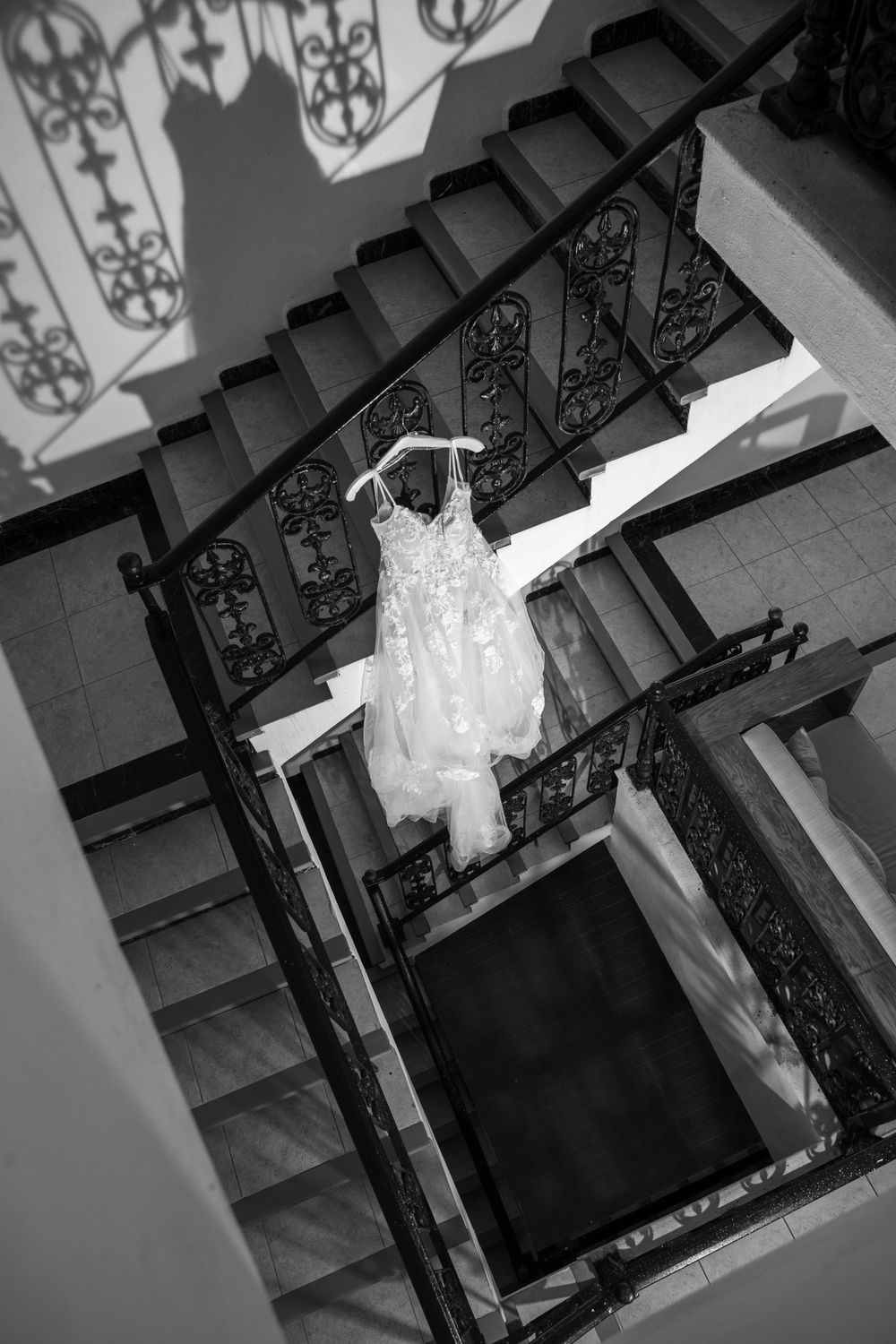 White lace wedding dress hanging on ornate staircase photographed in black and white.