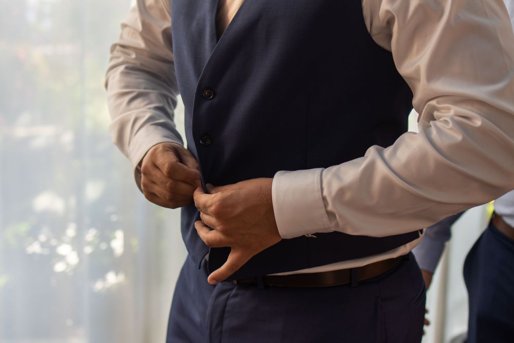 Someone helping another person adjust a formal navy vest.