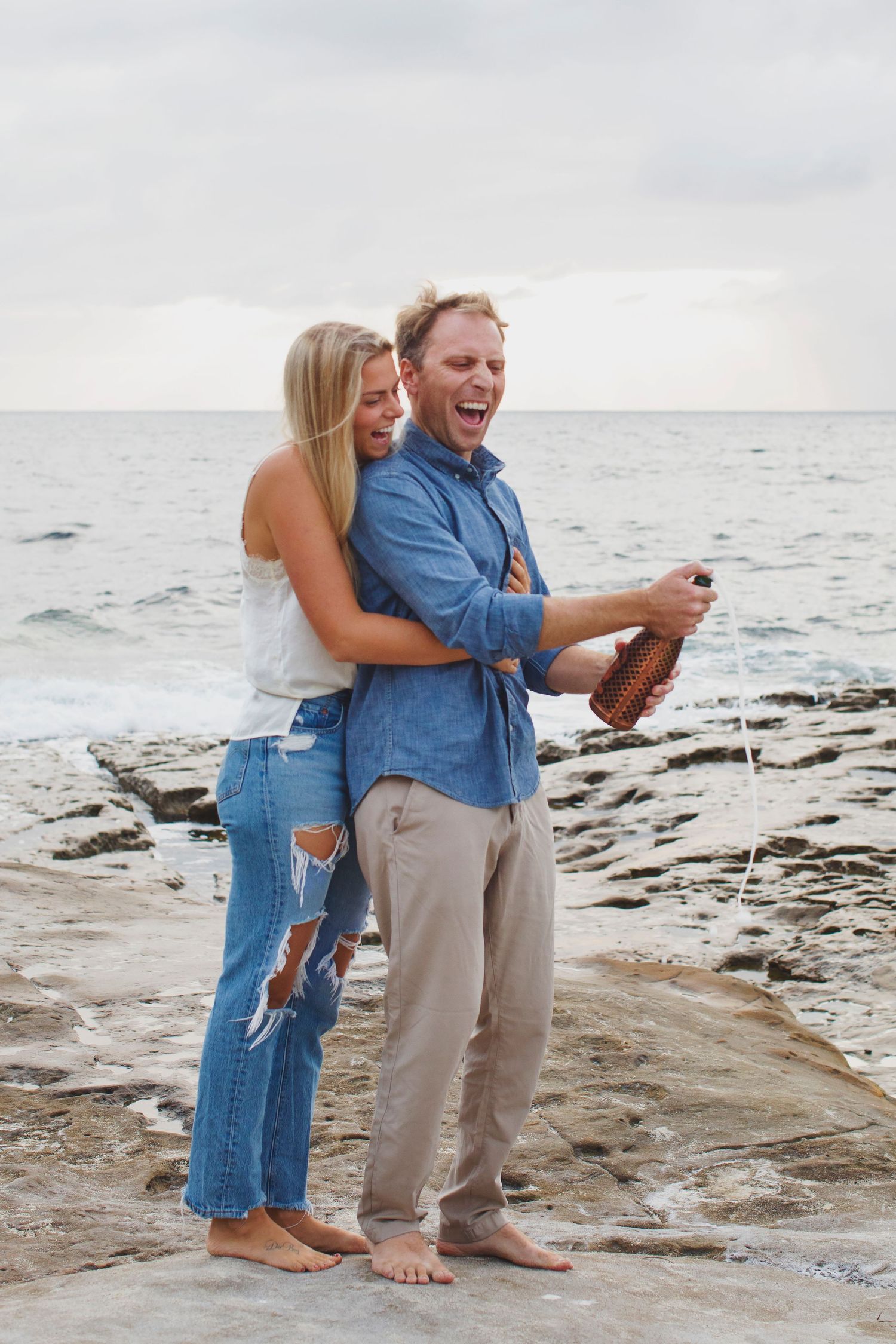 Celebration moment with champagne on rocky beach overlook.