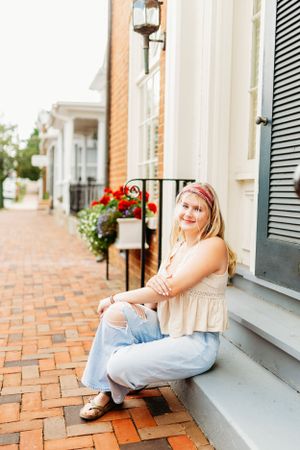 Smiling teen girl in ripped jeans sitting on steps along charming brick sidewalk.