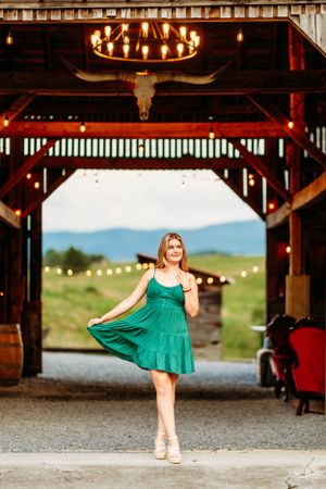 Young woman in green dress dancing under chandelier lights in rustic barn venue.