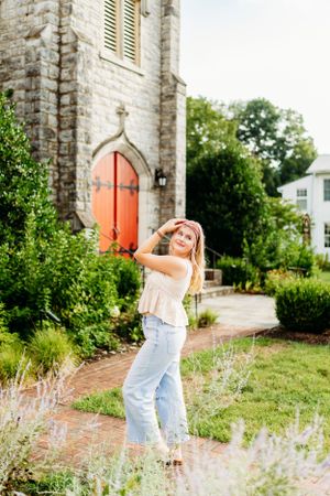 Young blonde woman posing in front of stone church with red doors.